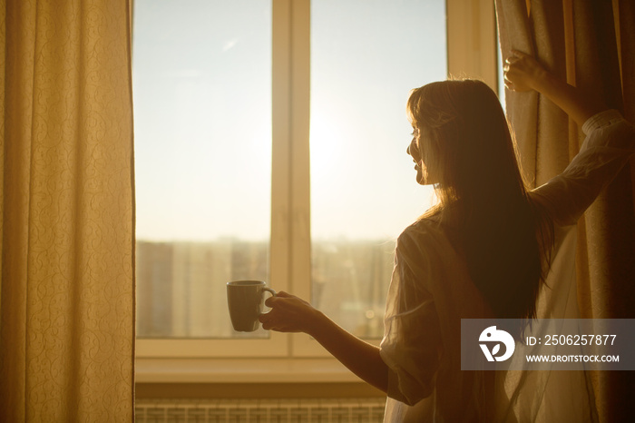 女人早上在窗边。迷人的性感女人与杯子