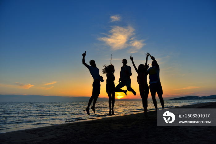 group of happy young people dancing at the beach on beautiful summer sunset