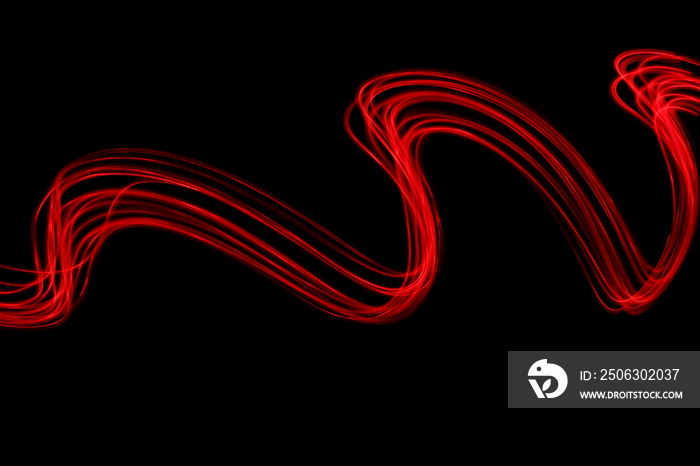 Long exposure photograph of neon red colour in an abstract swirl parallel lines pattern against a bl