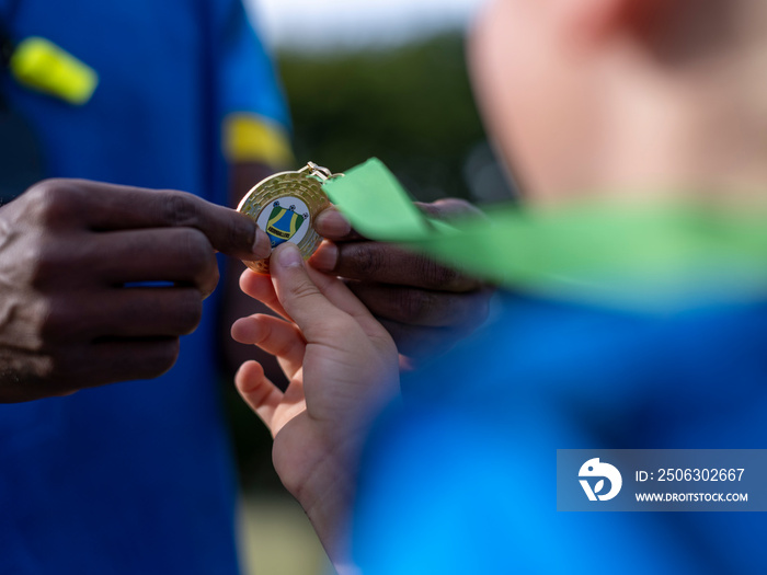 身穿足球服的女孩（8-9岁）从教练手中接过奖牌，特写