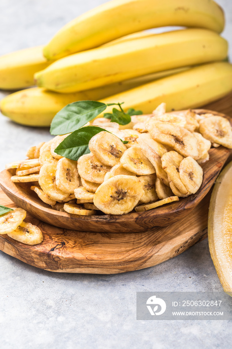 Homemade Dehydrated Banana Chips in a Bowl and fresh banana and slices on table