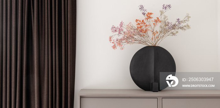 Dried colourful spring flowers in black hand glazed ceramic vase in nordic style against white wall.