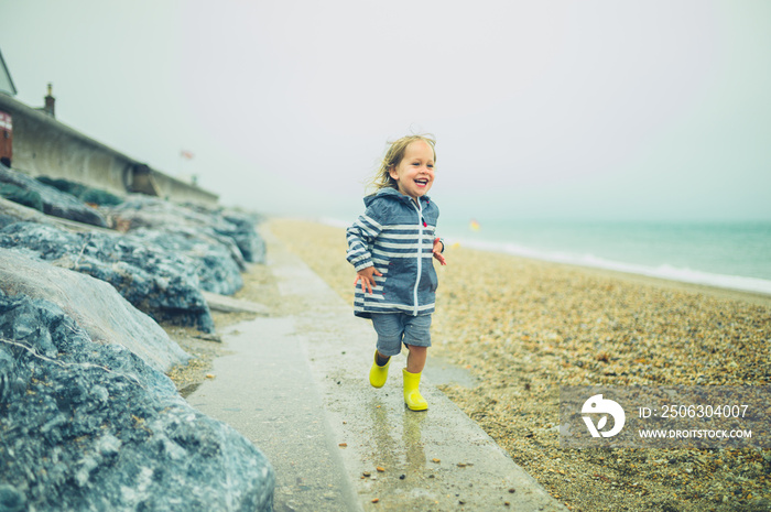 Little toddler running and playing on a rocky beach in the rain