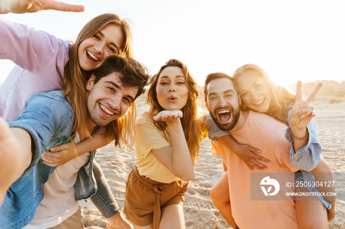 Image of young people smiling and taking selfie while walking on beach