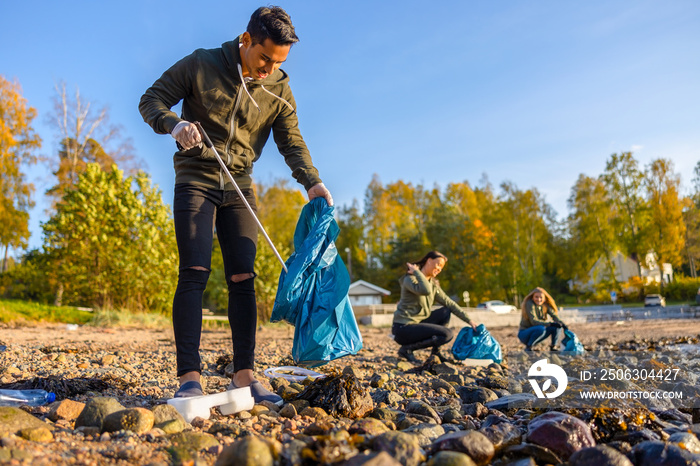 Focused man cleaning beach with group of volunteers on sunny day