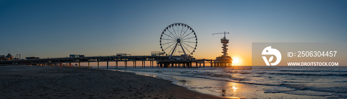 A panoramic shot of the sun setting beside the Pier in Scheveningen with the ferris wheel and the bu