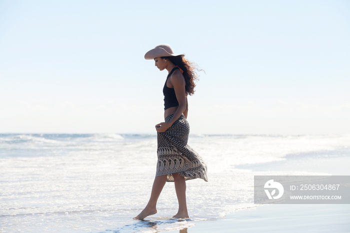 Woman in sun hat walking in sea against sky on sunny day