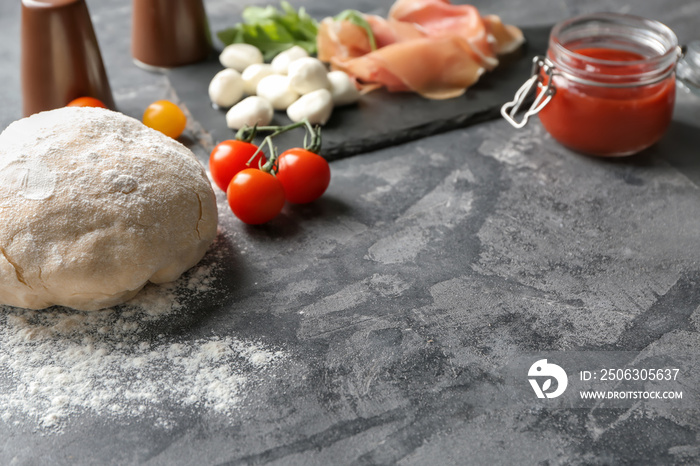 Raw dough and ingredients for pizza on grey textured background