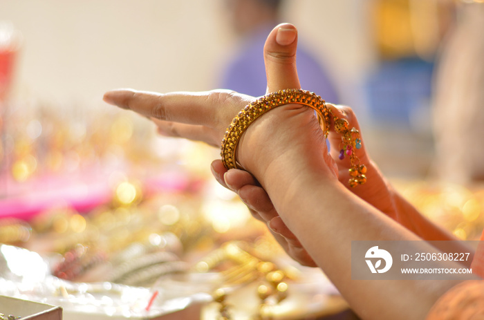 Indian woman trying bridal golden traditional wedding bangles in a shop in North India, New Delhi, I