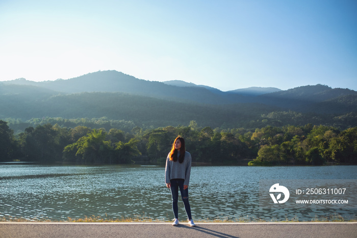 阳光明媚，一位美丽的亚洲女性独自站在湖光山色前的肖像