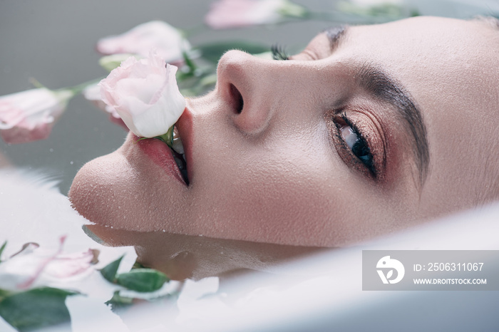 beautiful woman lying in clear water with flower in mouth