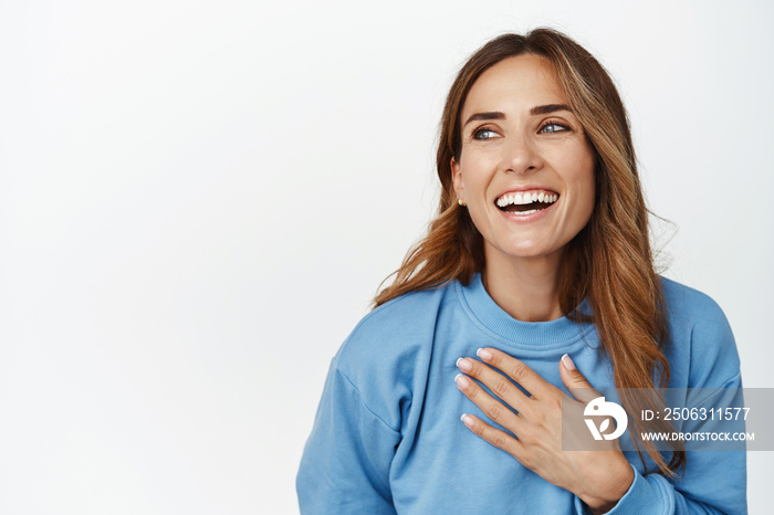 Close up portrait of beautiful brunette woman laughing, smiling and holding hand on chest, chuckle c