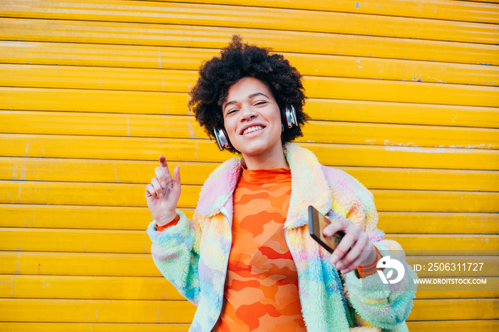 Young beautiful afro hair woman listening music holding smartphone dancing