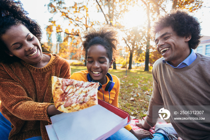 Mixed family having fun while picnicking in the park eating pizza.