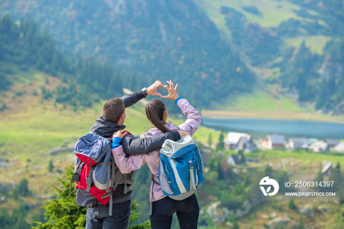 Two hikers at viewpoint in the mountains enjoying beautiful view of the valley with a lake.