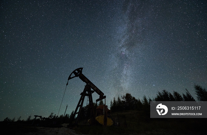 Operation of oil pump in borehole at night time under beautiful starry sky. Pumping natural fuel by 