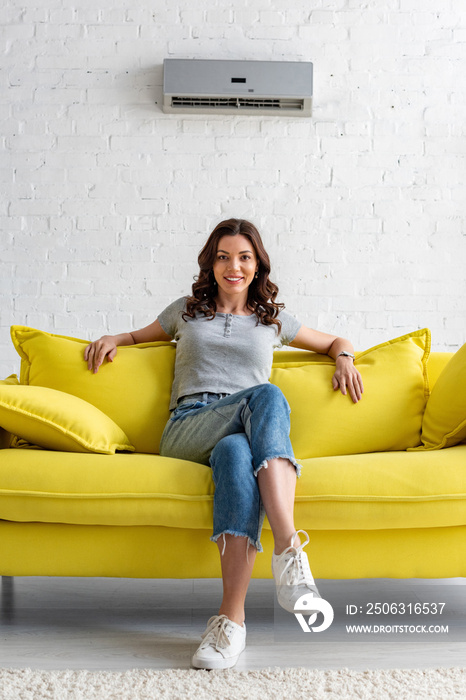 美丽微笑的女人坐在家里空调下的黄色沙发上