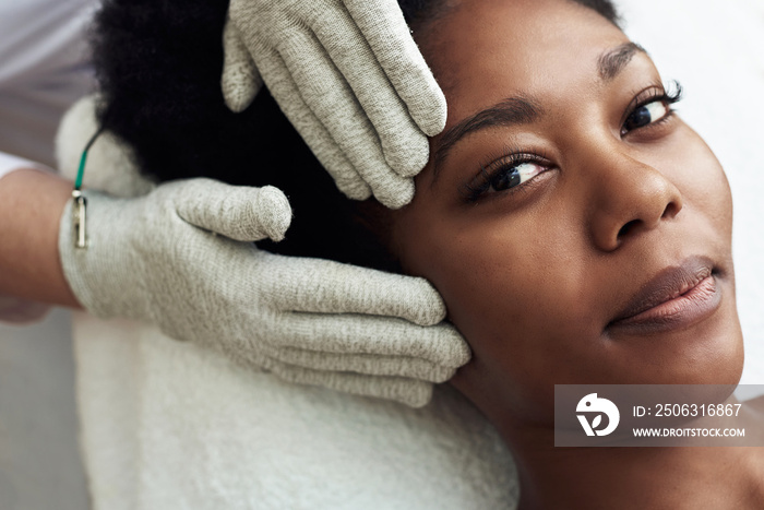 A dark-skinned model lies on the couch at the beautician and receives a microcurrent massage. Microc