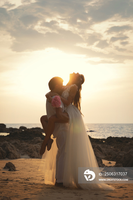 年轻的已婚夫妇拥抱在海滩上庆祝他们的婚礼