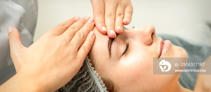 Young caucasian woman receiving facial massage by beauticians hands in spa medical salon