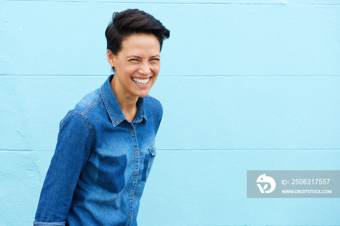 Young woman laughing against blue background