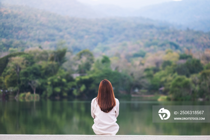 一位女士独自坐在湖边眺望群山，背后是绿色的自然