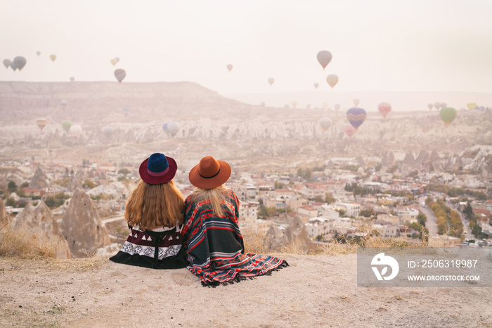 Traveling women wearing authentic boho chic style poncho, sweeter and hats looking on air ballons in