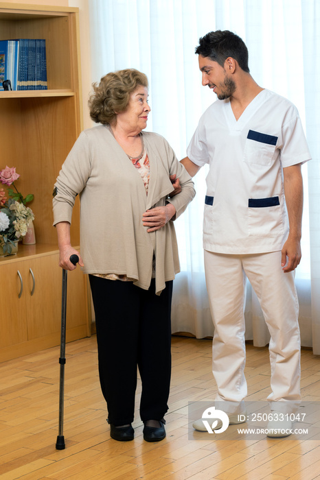 Senior woman with cane standing next to young male nurse at home.