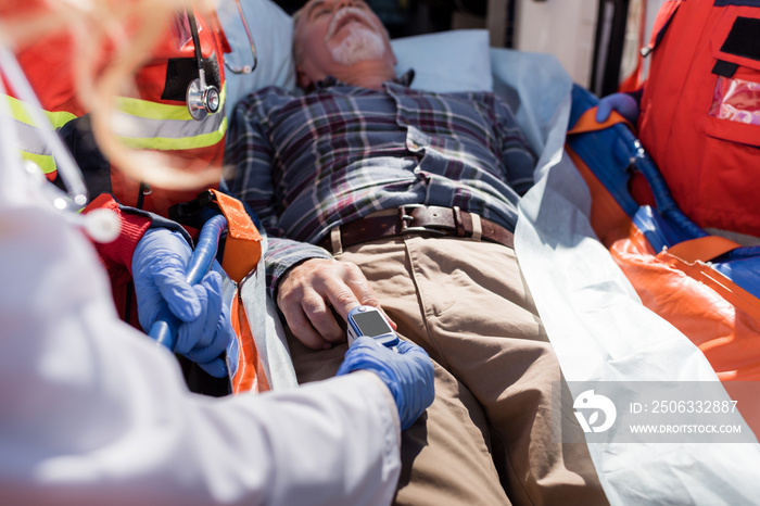 Selective focus of doctor fasting heart rate monitor on patient near paramedics and ambulance car