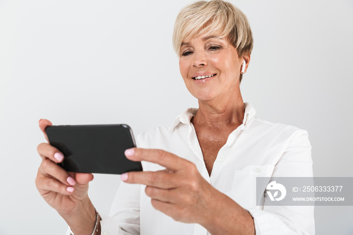 Image of happy adult woman with short blond hair wearing earpods and holding cellphone