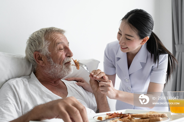 senior man with smiling nurse, takes care breakfast and discussion and cheer on bed at nursing home