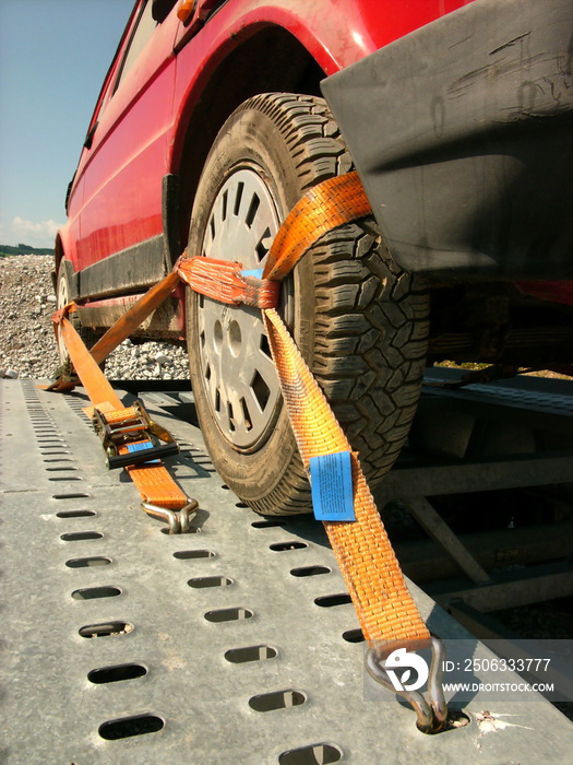 Mit Spanngurt gesichertes Rad eines alten Kleinwagen auf dem Lochblech des Anhänger nach der Panne i