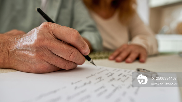 Man writing letter on paper near his blurred wife