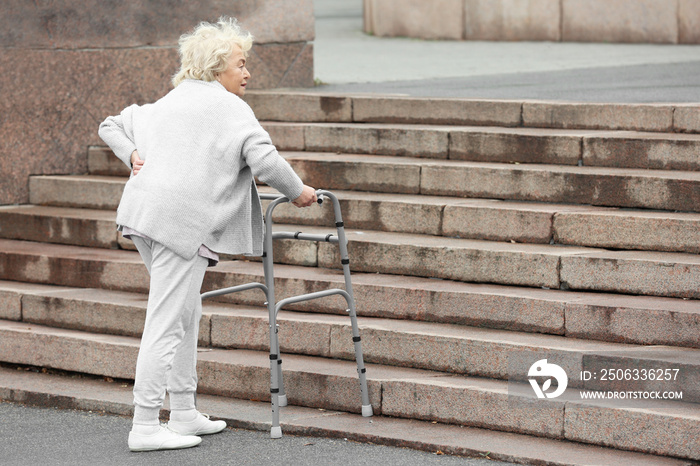 老年妇女带着步行架在户外上楼梯