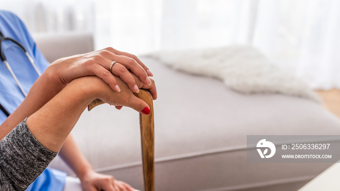 Close-up of woman using cane assisted by physiotherapist. Young woman and old woman holding hands. C