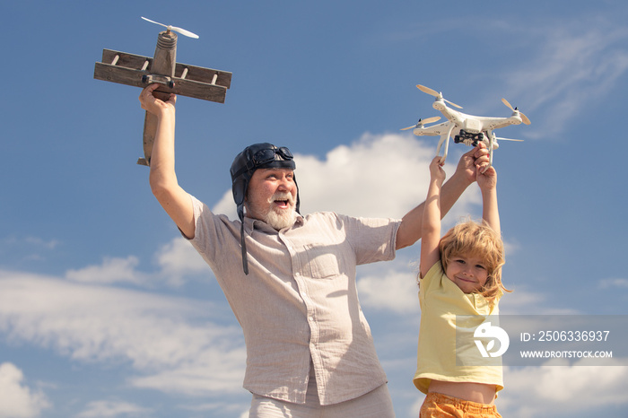 Young grandson and old grandfather playing with toy plane and quadcopter drone against sky. Child pi