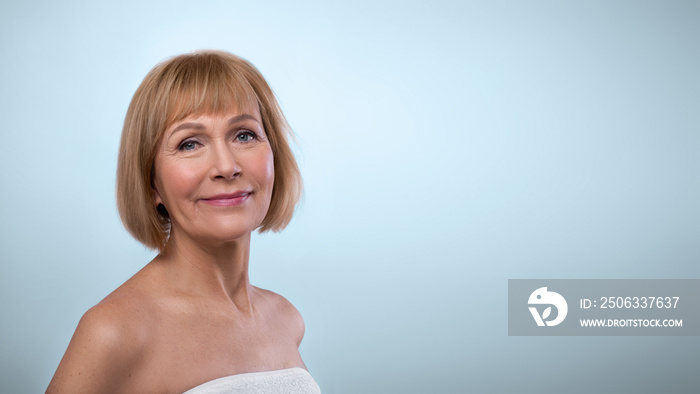 Natural beauty. Portrait of feminine senior woman in towel having smooth silky skin, posing on light