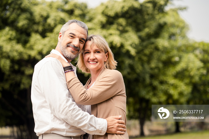 Senior elder Caucasian couple sitting on ground together in park in Autumn. Wife hugging husband fro