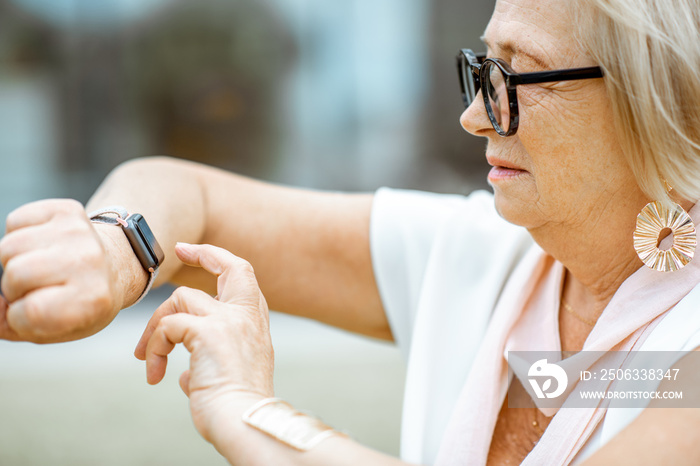 Senior woman using smart watch outdoors. Concept of using modern technologies by elderly people