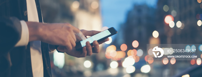 Closeup image of male hands with smartphone at night on city street, searching internet or social ne