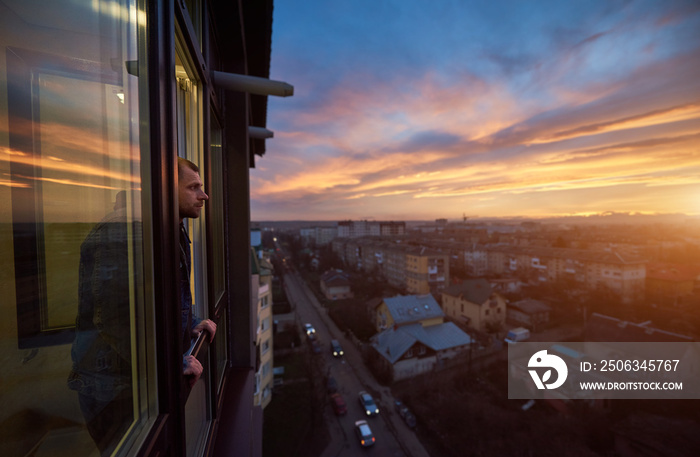 成年男子站在阳台上眺望远方，欣赏日落。美丽的城市土地