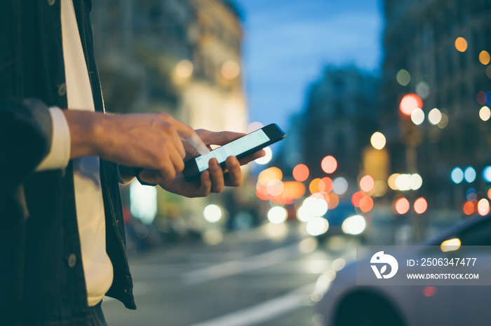 Closeup image of male hands with smartphone at night on city street, searching internet or social ne