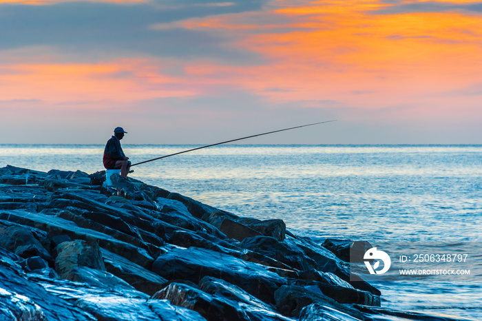 Angler fishing on the sea shore at sunrise