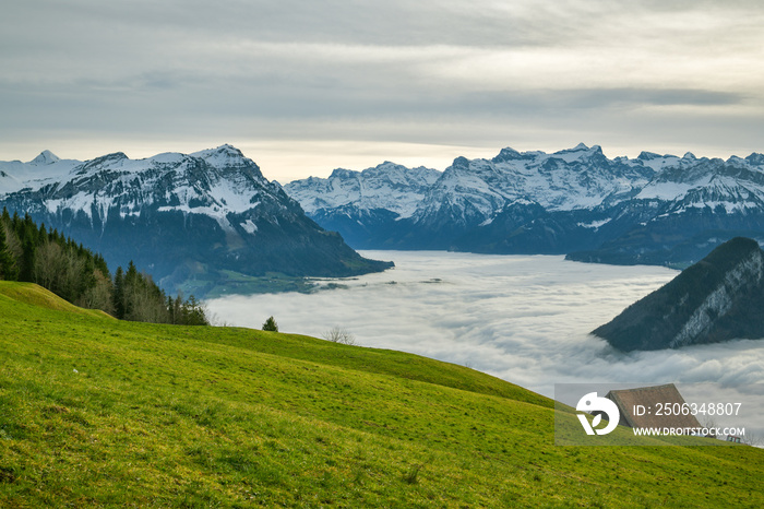 Clouds covering lakes below majestic Alpine peaks as seen from small meadow above the Sattel