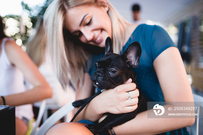 Beautiful young woman sitting in cafe with her adorable French bulldog puppy. Spring or summer city 