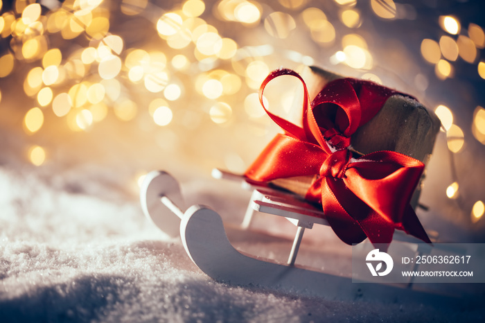 Toy wooden sledge with gift standing in snow. Christmas