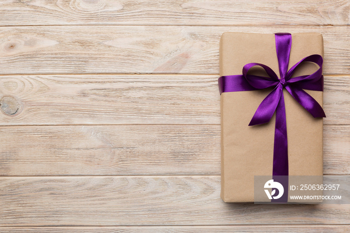 Holiday gift box wrapped in craft paper with colored bow on table background. Top view, flat lay, co