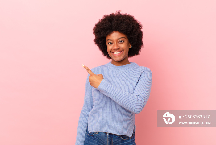 afro black woman smiling cheerfully, feeling happy and pointing to the side and upwards, showing obj