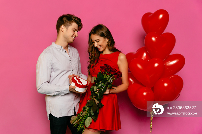 Attractive man gives red roses and making sweet present for her gorgeous girlfriend, dressed in red 