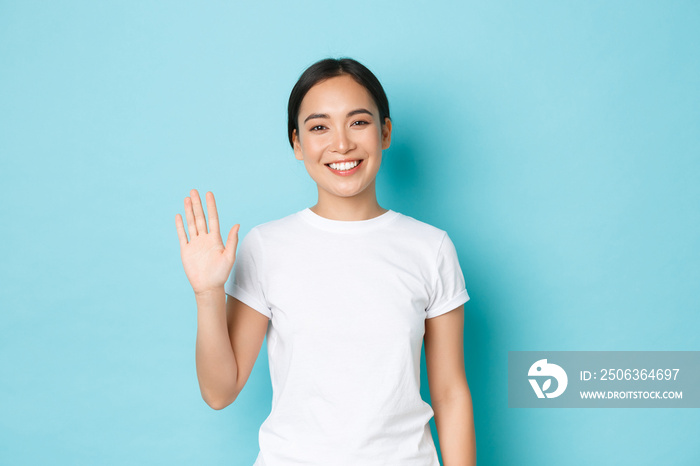 Portrait of friendly cheerful asian girl in white t-shirt saying hello, greeting people, smiling and